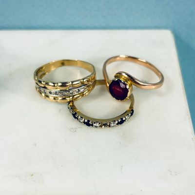 trois bagues en or, ornées de diamants et d'un grenat, reposent sur une dalle de marbre