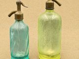 deux bouteilles en verre vertes et bleues munies d'un robinet en métal sur le dessus