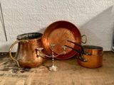 Plusieurs casseroles et poêles en cuivre sont posées sur une table en bois