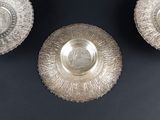 three silver plates with a design on them on a black surface