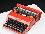 a red typewriter sitting on top of a white sheet of paper