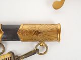 a gold and black sword with a keychain on a white surface