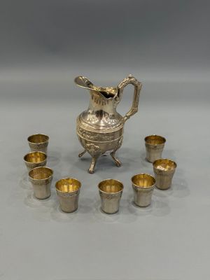 an image of a silver pitcher and six cups on a table