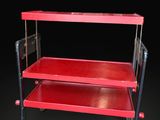 a red metal trolley with two shelves and a black background