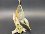figurine en porcelaine représentant un oiseau perché sur une branche, sur fond gris