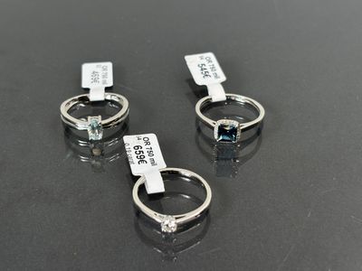 trois bagues ornées d'une topaze bleue et d'une topaze blanche reposent sur une surface noire