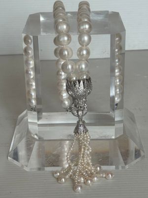 un collier de perles blanches muni d'un fermoir en argent, présenté sur un support transparent