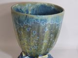 un vase bleu et vert posé sur une surface blanche