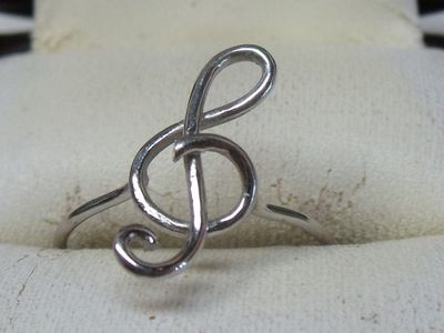 une bague en argent avec une note de sol au centre, posée sur un tissu blanc
