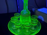 une carafe à liqueur en verre vert fluo, accompagnée de six verres et d'une autre carafe, le tout présenté sur un plateau