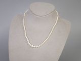 un collier de perles blanches sur un mannequin, muni d'un fermoir en argent