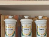 trois bocaux blancs posés sur une étagère, avec des livres en arrière-plan