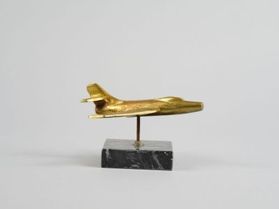 une image représentant un avion doré posé sur un socle en marbre noir