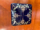 a black plate with flowers on it sitting on a wooden table