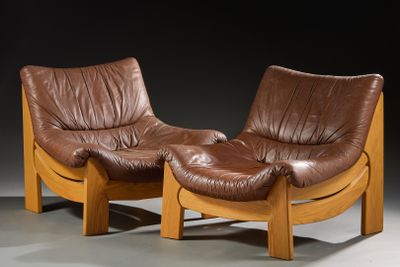 une paire de fauteuils en cuir marron aux pieds en bois, dans une pièce sombre