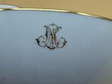 someone is holding a white bowl with a gold rim and a monogram on it