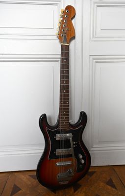 une guitare électrique posée sur un parquet, près d'un mur blanc