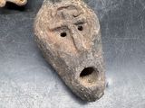 three clay masks are sitting on a metal surface, one of which is shaped like a man ' s face and the other of which is shaped like a dog '