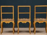 pair of gold chairs with upholstered seats against a blue wall