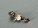a close up of a pearl and sapphire broochle on a gray surface