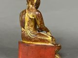 a gold statue of a seated buddha sitting on a red block