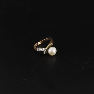 a gold ring with a pearl and diamonds on a black surface