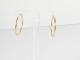 une paire de boucles d'oreilles créoles en or posée sur un présentoir transparent