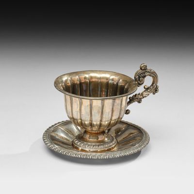 une tasse et une soucoupe en argent posées sur une soucoupe, elle-même posée sur une autre soucoupe