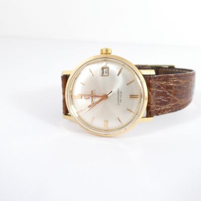une montre en or avec un cadran blanc et un bracelet en cuir marron