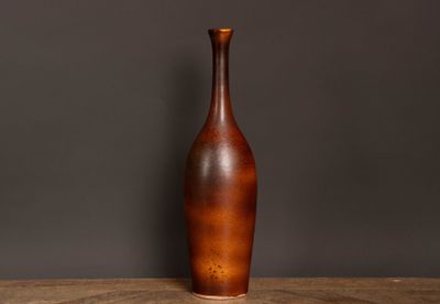 un vase marron posé sur une table en bois devant un mur gris