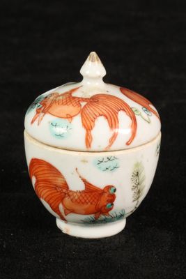 an orange and white bowl with fish on it on a black surface