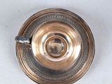 silver plated tea cup with a saucer on a white surface