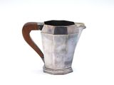 a silver pitcher with a wooden handle on a white surface