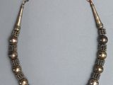 un collier composé de perles en laiton et en argent, avec une perle rouge