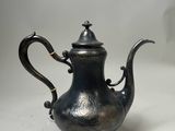 une théière ancienne en argent, dotée d'une anse noire sur un fond blanc