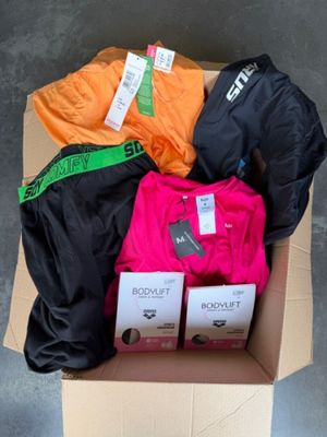 une boîte en carton remplie de vêtements divers, posée par terre