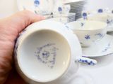 a person holding a cup and saucer in front of a stack of plates