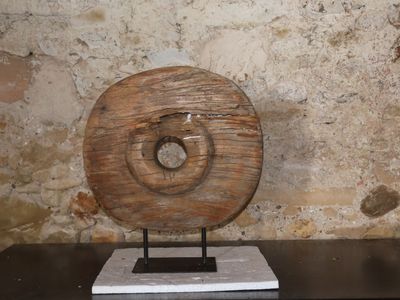 une sculpture en bois posée sur un socle devant un mur de pierre