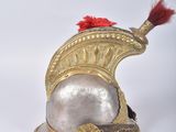silver and gold helmet with a red feather on top of it