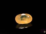 un diamant jaune de forme ovale posé sur une surface réfléchissante avec un fond noir