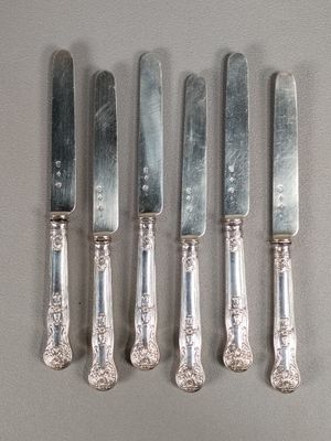 six couteaux en métal argenté et un porte-couteaux posés sur une table