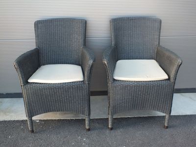 une paire de chaises en osier gris avec des coussins blancs, placées devant une porte de garage