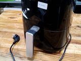 une friteuse à air chaud Philips posée sur une table en bois, dont le cordon d'alimentation est branché
