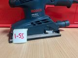 un gros plan d'une ponceuse filaire posée sur une table, avec une boîte rouge en arrière-plan