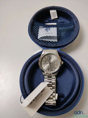 une montre en argent dans un étui bleu, sur lequel est accrochée une étiquette