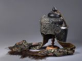 un casque en argent et en or posé sur un socle, orné d'une longue chevelure