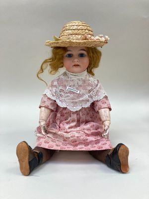 poupée assise sur une surface blanche, vêtue d'une robe rose et d'un chapeau de paille
