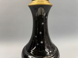 un vase noir orné d'un couvercle doré, posé sur une table blanche