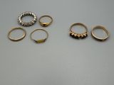 trois bagues en or et deux bagues en argent posées sur une table
