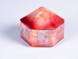 une boîte rouge et rose avec un couvercle, posée sur une surface blanche